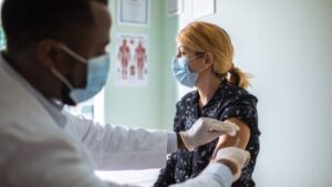 A masked doctor gives a COVID-19 vaccine to a masked patient.