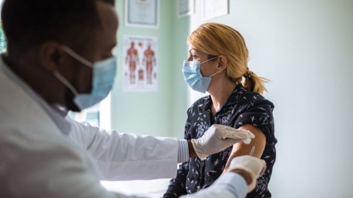 A masked doctor gives a COVID-19 vaccine to a masked patient.