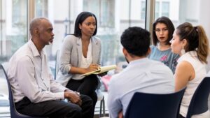 A group therapy session contains several adults sitting in a circle.