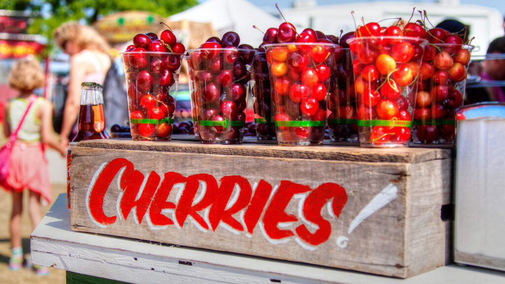 Several plastic cups filled with cherries rest on a crate labeled, "Cherries!"