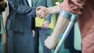 A person using forearm crutches shakes hands with another professional.