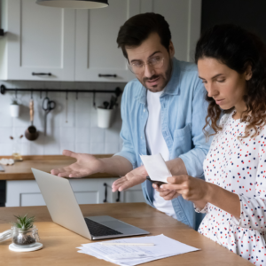 A couple discusses medical bills in their kitchen.