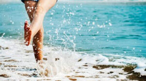 A person runs through the waves on a sandy beach.