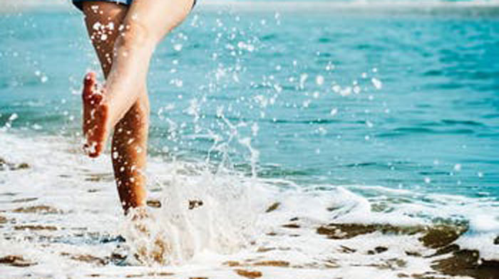 A person runs through the waves on a sandy beach.