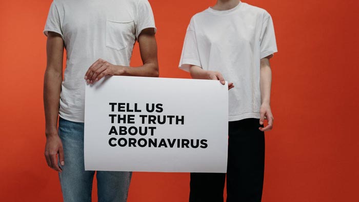 Two people in white shirts hold up a sign that reads, "Tell us the truth about Coronavirus."