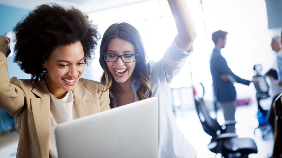 Two women celebrate something they see on their laptop screen.