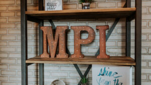 Three industrial-style metal letters rest on a shelf. They read, "MPI."