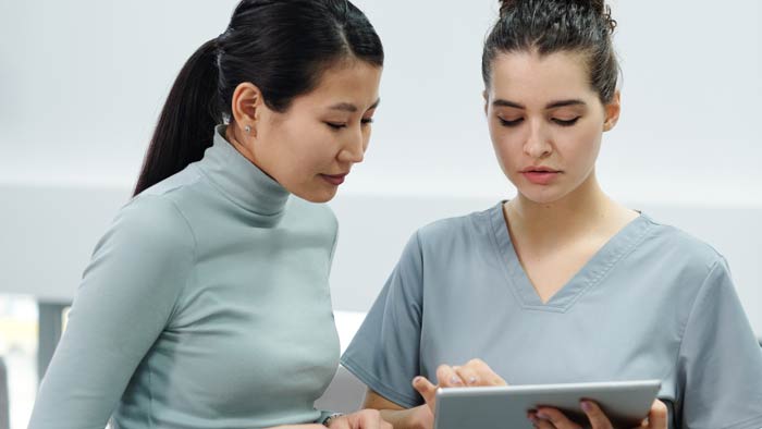 A woman speaks with a doctor, who shows her something on a tablet screen.