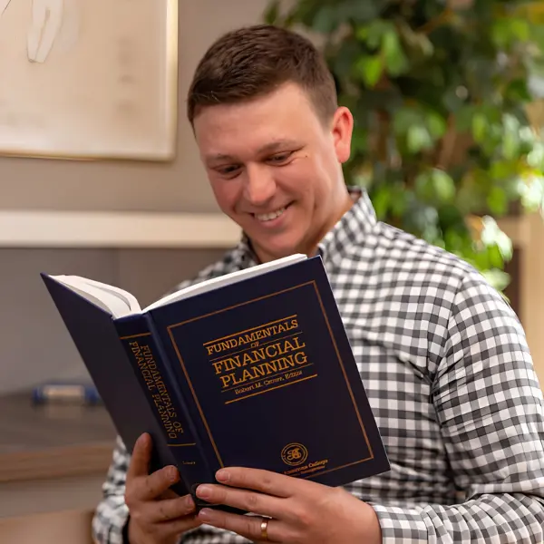 A member of the Michigan Planners team smiles while reading a book titled, "Fundamentals of Financial Planning."
