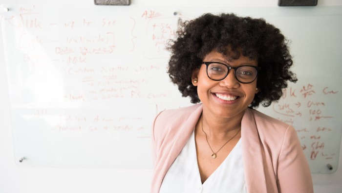 A woman smiles in front of a white board that's filled with equations.