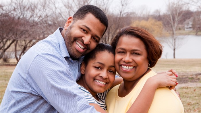A father, mother, and daughter all embrace while smiling.