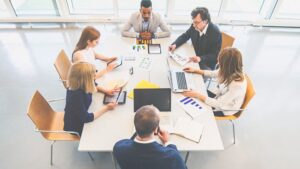 A team of coworkers works around a table. They have laptops, graphs, tablets, and other useful tools.