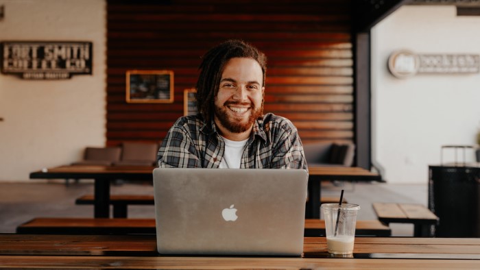 A man smiles from behind his laptop.