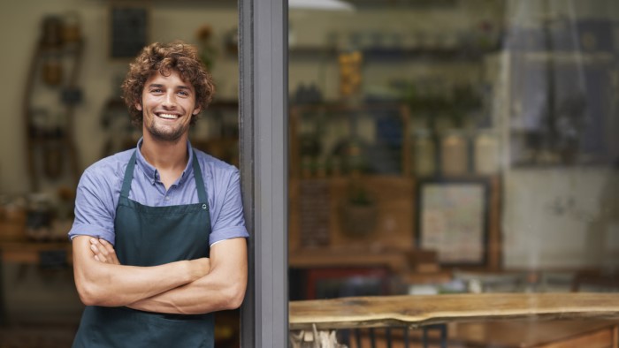 A man smiles while leaning against the wall at his work.