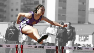 A female athlete jumps over a hurdle.