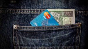 A debit card and $100 bill stick out of someone's jeans pocket.