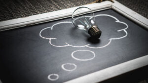 A light bulb rests on a chalkboard. Chalk has been used to draw a thought bubble around it.