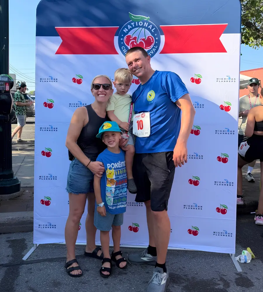 A mother, father, and two sons pose in front of the Traverse City Cherry Festival sign.