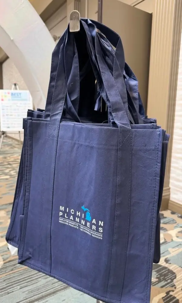 Tote bags hang on a hook. They each feature the Michigan Planners logo.
